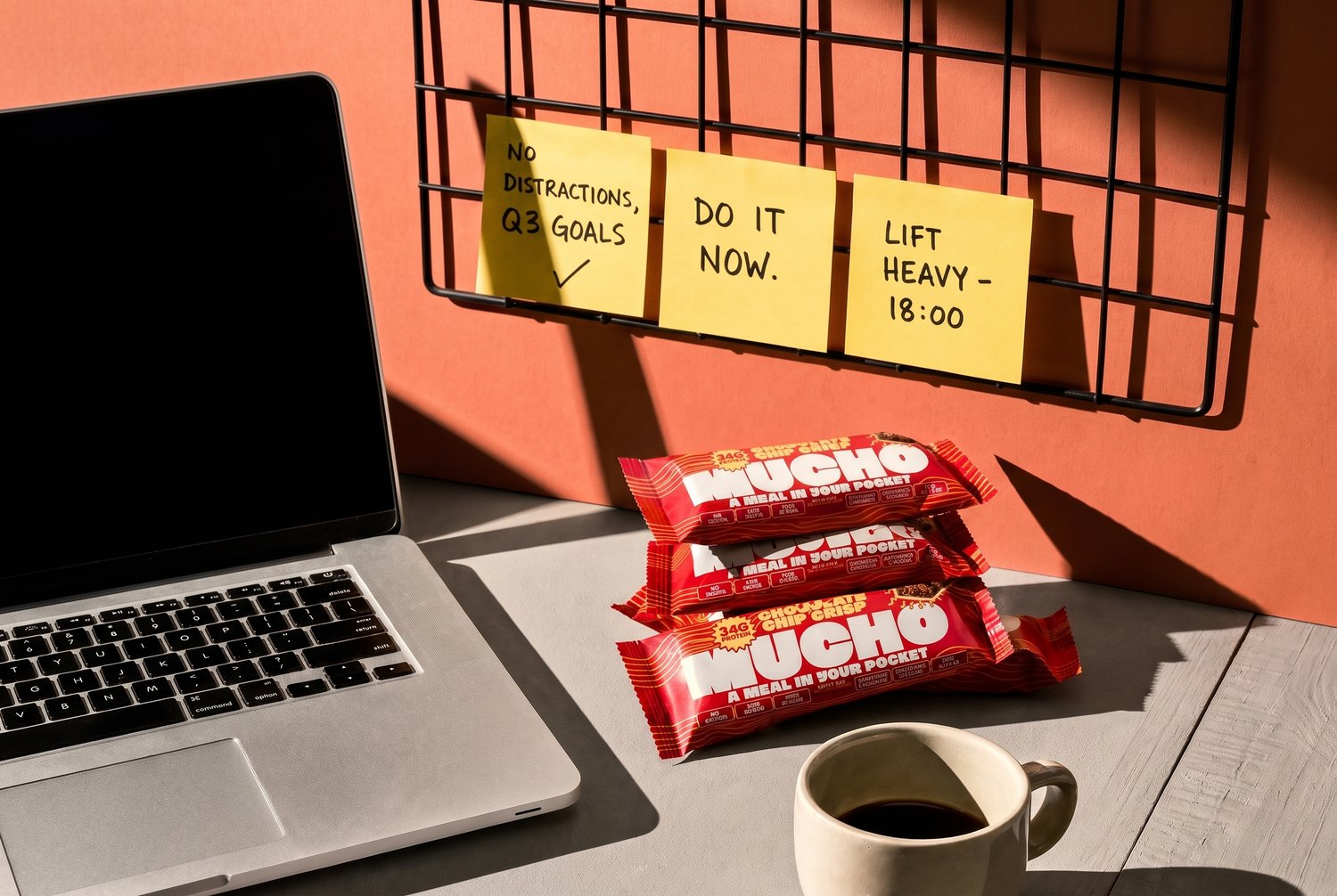 Mucho meal replacement bars stacked on a desk with coffee, a notebook and sticky notes